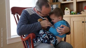 A father tickles his toddler in a rocking chair in house