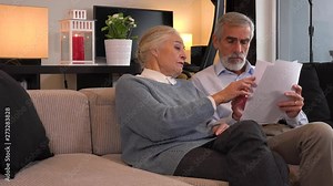 An elderly couple sits on a couch in an apartment and goes through papers