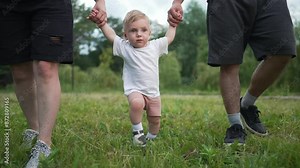Toddler first steps with family. Parents holding Toddler hands while learning to step. Family bonds in nature. Joyful moments as baby learns to step. Family celebrates milestone of learning to step.