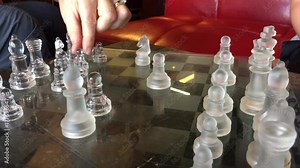 Glass chess game close up in coffee shop with hands moving pieces to various areas on board.