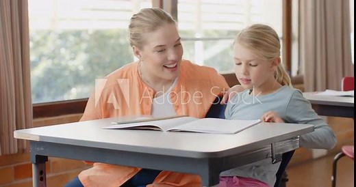 In school, female teacher smiling and helping young student with homework at desk