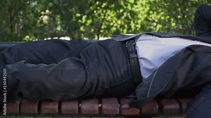 Adult man is sleeping at the bench at the park