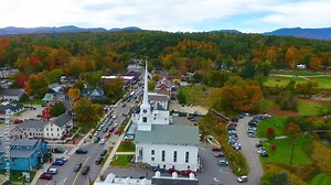 Aerial pan across beautiful small Vermont town of Stowe in peak fall foliage with focus on church