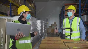 warehouse worker wearing medical face mask pulling a pallet truck parcel moving to dispatch . manager woman checking order with laptop in distribution warehouse. during coronavirus,covid-19 pandemic
