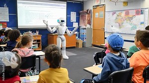 A humanoid robot interacts with a class of children, demonstrating technology and fostering curiosity in an educational setting