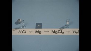 United States CIRCA 1950s: two test tubes with liquid, one bubbling, near magnesium sample, chemical equation HCL + MG = MGCL2 + H2, hand puts styrofoam balls with "CL" and "H" near the HCL