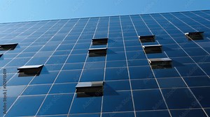 Close shot of some open windows in an office building with the blue sky as background and a glass facade. Camera pan movement from the left side.
