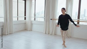 Young beautiful ballerina dancing gracefully in a spacious studio during rehearsal at daytime, performing classical ballet steps and turns. Full length shot