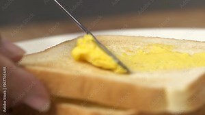 Close up spreading butter on a piece of bread.