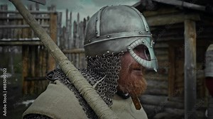Medium close-up tilt shot of middle-aged medieval male warrior with red beard, in chainmail, iron helmet, battle axe on shoulder, standing in fortress yard, watching companions practice and grinning