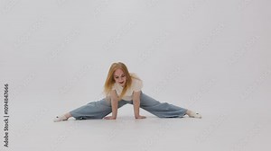 Woman in jeans and white shirt is doing splits in a white room