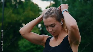 Caucasian athlete woman ties her ponytail before the training, wearing smartwatch tracking her calories on the park background. People and sport concept.