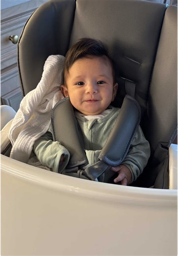 Happy cute baby smiling in high chair wearing green outfit mealtime fun
