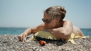 A young woman in a swimsuit is sunbathing on the beach and stacking pebbles.