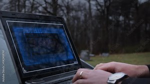 A hitman or assassin types on a laptop to activate a bomb