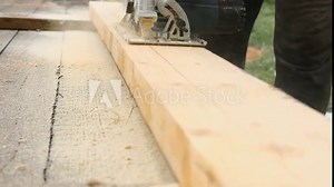 Male carpenter using electric circular saw in backyard workshop with wood chips flying. Building contractor worker cutting plank by fretsaw tool to cut boards on new home construction project. Sawing