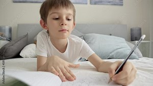 Little boy working on his homework in bed, writing in a notebook. Concepts of education, child development, and remote schooling from home