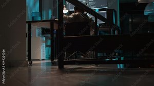 Young programmer with disability typing source code on terminal window, displayed on multiple screens. IT coder wheelchair user programming new user interface in office late at night. Tripod shot.