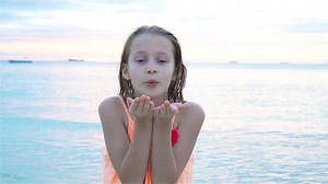 Adorable little girl at beach having a lot of fun in the evening. Happy kid looking at camera background beautiful sky and sea