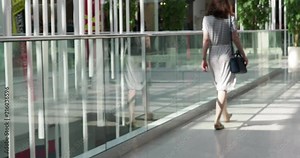 Rear view of cheerful beautiful woman walking in shopping center. Young female in striped dress walking in trade centre. 4k video