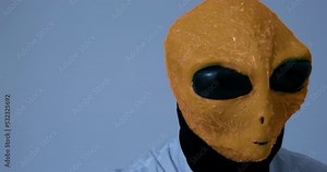 Extraterrestrial in a white coat and sterile gloves shows a jelly worm and then gives it to someone, front view. Portrait of an actor in a mask and alien costume, friendly prank.