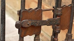 Ancient metal rusty wrought handle deadbolt (latch) of closed door of the lattice gate of the antique cathedral in Spain closeup. Mechanical medieval lock