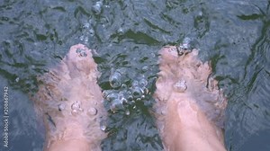 Relaxing for life, natural therapy concept : Young man's feet standing on rocks with clear, cold water. Feel comfortable and relax in nature of forest with water flowing on summer day, slow motion
