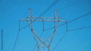 Close up: top of high voltage power transmission tower and electricity pylon with wires against blue sky. Power pole
