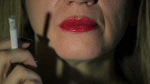 Woman smokes cigarette and exhales smoke in camera. Extreme close up