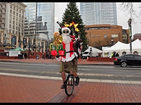 Santa plays flaming bagpipes with one hand while holding a pile of presents in downtown Portland