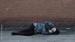 Bearded homeless lies down on ground to sleep. Tramp in dirty clothes, hat cap. Below poverty line. Fugitive beggar. Illegal immigrant. Consequences of drunkenness, alcoholism. Male refugee needs help