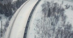 Freight train with coal on Trans Siberian winding two-sided railways near river at winter frozen day in Ural Mountains in Russia - Aerial drone view