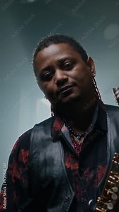 Vertical view of African American saxophonist playing instrument, then stopping and posing for camera with straight face at rehearsal in music studio