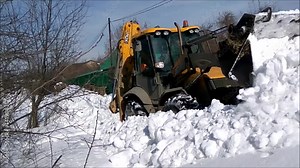 Tractor plowing snow on street. Red farm tractor with snowplow equipment removing snow from streets in snow blizzard.