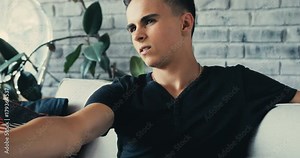 Close up face serious young man watching the TV sits on the sofa with remote in his hands to find something on television at home portrait Slow Motion Shot. Shot on RED EPIC camera