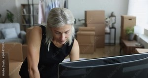 Serious senior entrepreneur lady using computer in home office, storage place. Mature business woman using retail internet application on desktop, working on online store order