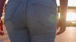 Rear View of a Slender Woman in Jeans Walking through a City Park...