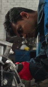 Mechanic in red gloves uses pneumatic tool on engine block in industrial workshop, performing precise mechanical repair, focused worker in blue uniform adjusts engine components