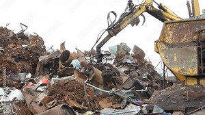Sorting and loading of scrap metal. / Excavator is loading scrap metal junk into a bin at a garbage dump or recycling center.