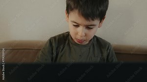 Serious little boy with laptop computer on sofa at home, surfing the web, typing on keyboard. New technology education concept.