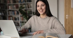 Novedades de estudiante universitario Z de gen fresco enfocadas escribiendo notas, resumen de lección, usando laptop en biblioteca pública, escribiendo, viendo webinar, clases en línea, girando la cara, mirando la cámara, sonriendo