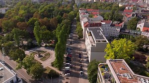 Aerial view of a street in Berlin with cars parked on the side of the road and an urban park with a roundabout and a statue