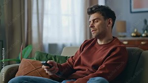Nervous guy switching television channels on couch with controller close up.