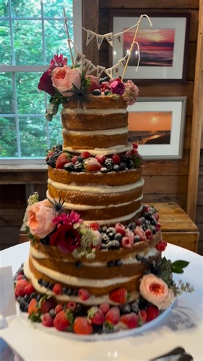 Artisan Bake Shop | Cake Bakery Massachusetts on Instagram: "A torte-style vanilla naked wedding cake that proves rustic can still be breathtaking ✨ This cake features soft, exposed vanilla cake layers filled with a rich cream cheese buttercream, then finished with an abundant cascade of fresh raspberries, strawberries, blueberries, and blackberries. Delicate fresh florals in peach and berry marsala tones add movement, texture, and that effortlessly romantic Cape Cod feel. Designed to look inten