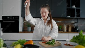 Young woman cooking, dancing at kitchen. Girl cook food listen music with headphones and dancing in modern kitchen. Girl with vegetables play radio and dance, while cooking salad have fun at home.