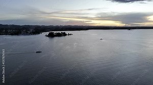 Drone flies to the right over Lake Peten Itza, facing the sunset and following ferry boats as they cross in Flores, Guatemala