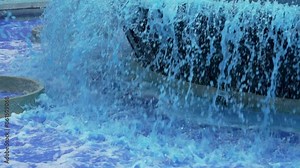 Blue colored water of urban outdoor cascading waterfall fountain with falling cool tinted liquid close up