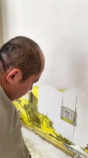 is repairing a damaged wall near an electrical outlet using plaster and tools.