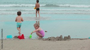 Little girl with brothers are building a sand castles on the beach