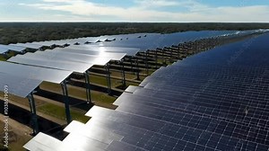 Drone footage sweeping across a solar farm, capturing massive solar panels slowly tilting and rotating to follow the sun throughout the day.